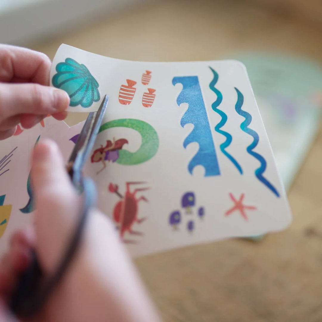 Girl holding scissors cutting out mermaid and aquatic animals temporary tattoos from the sheet of tattoos from Great Pretenders 