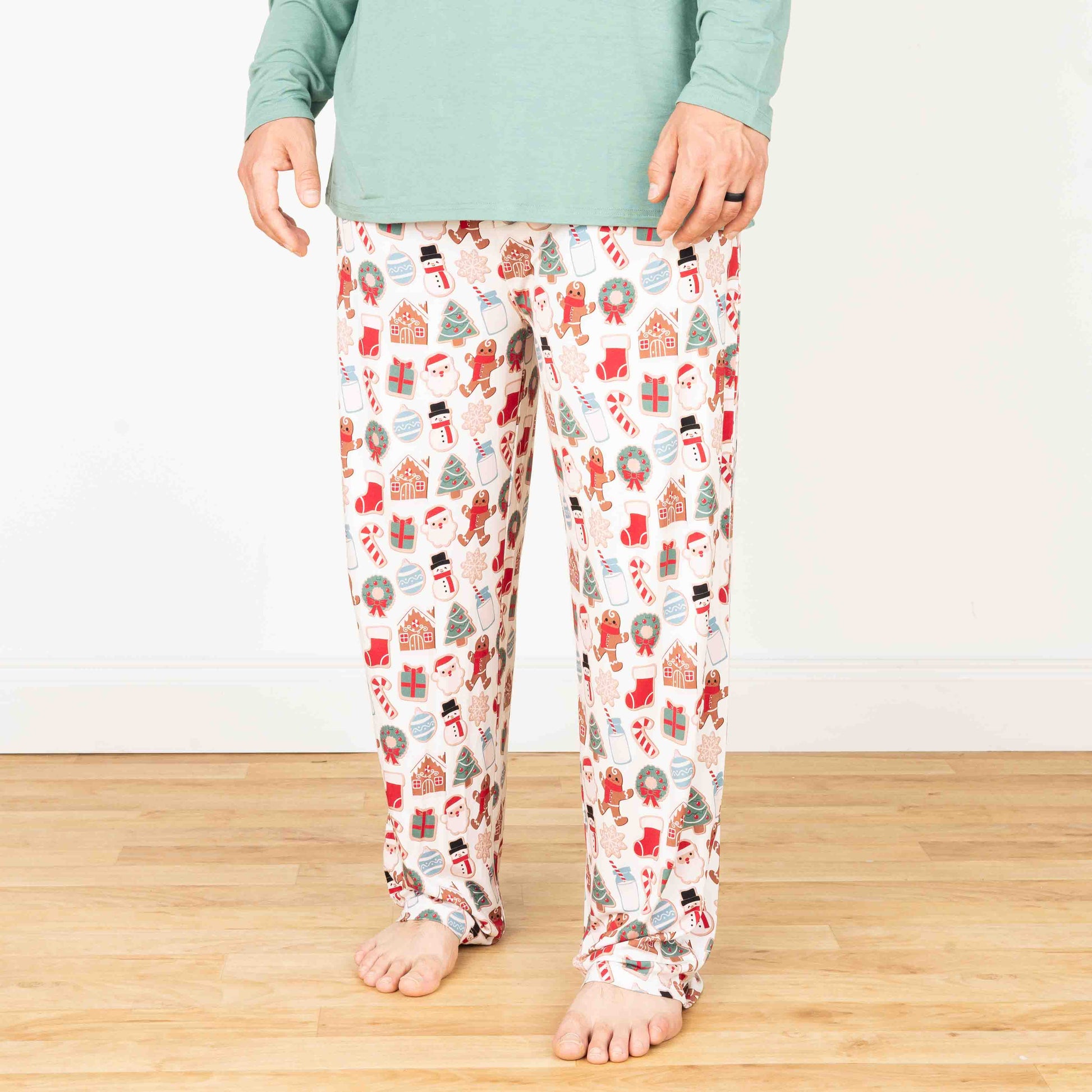 A person standing wearing Christmas-themed bamboo lounge pajama pants with a variety of festive prints including cookies, presents, and holiday decorations.