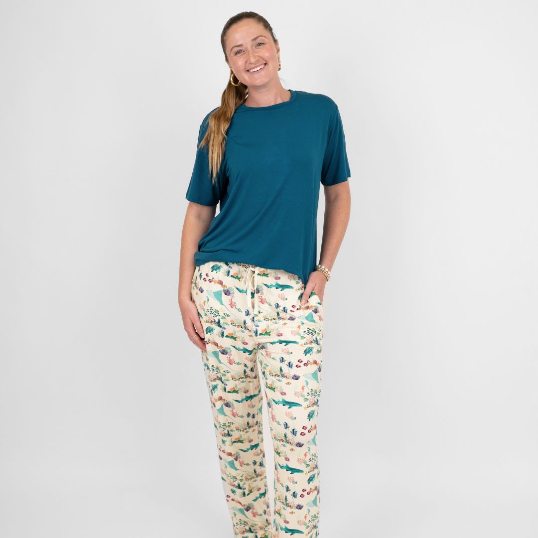 Woman smiling and wearing our Emerson and Friends Coral Reef Bamboo Relaxed Lounge Pajama Pants, featuring a serene ocean-inspired print with sea turtles, sharks, coral, and tropical fish on ultra-soft bamboo fabric perfect for all-day comfort and night.