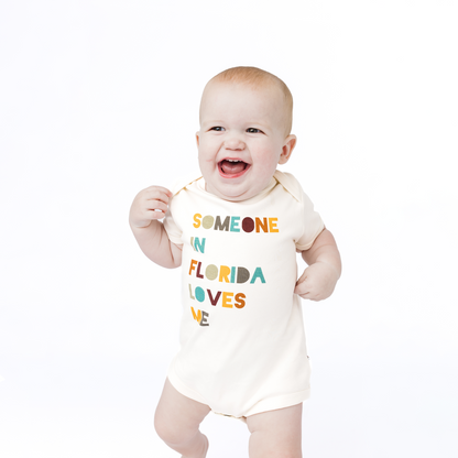 Baby wearing a onesie with colorful text on a white background