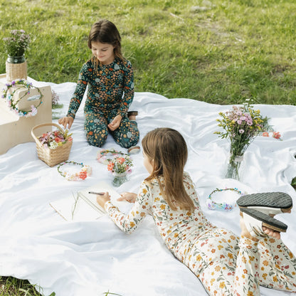 Two girls wearing matching floral bamboo pajamas while making flower crowns outdoors.