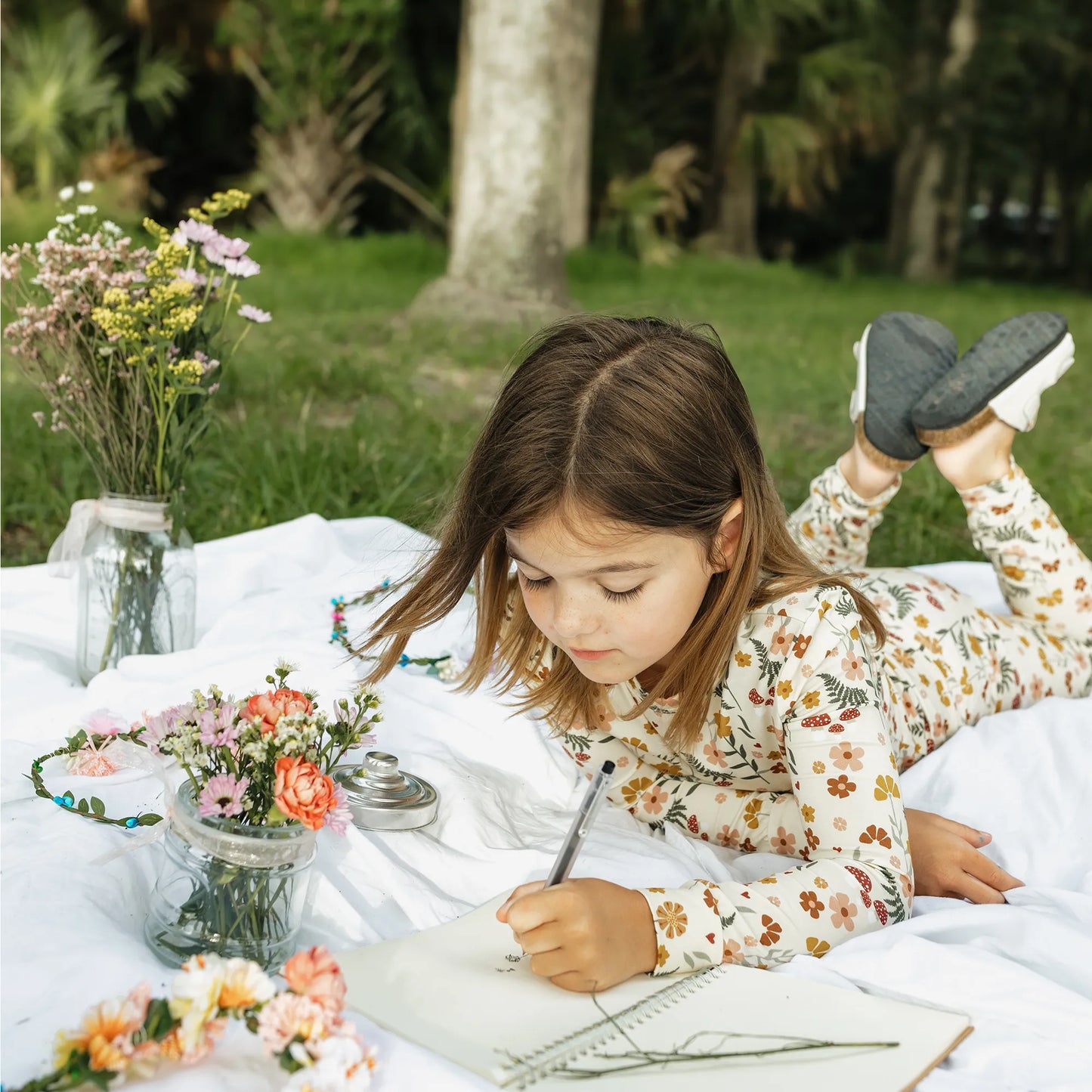 girl wearing cream pj set with floral print on greenery background.