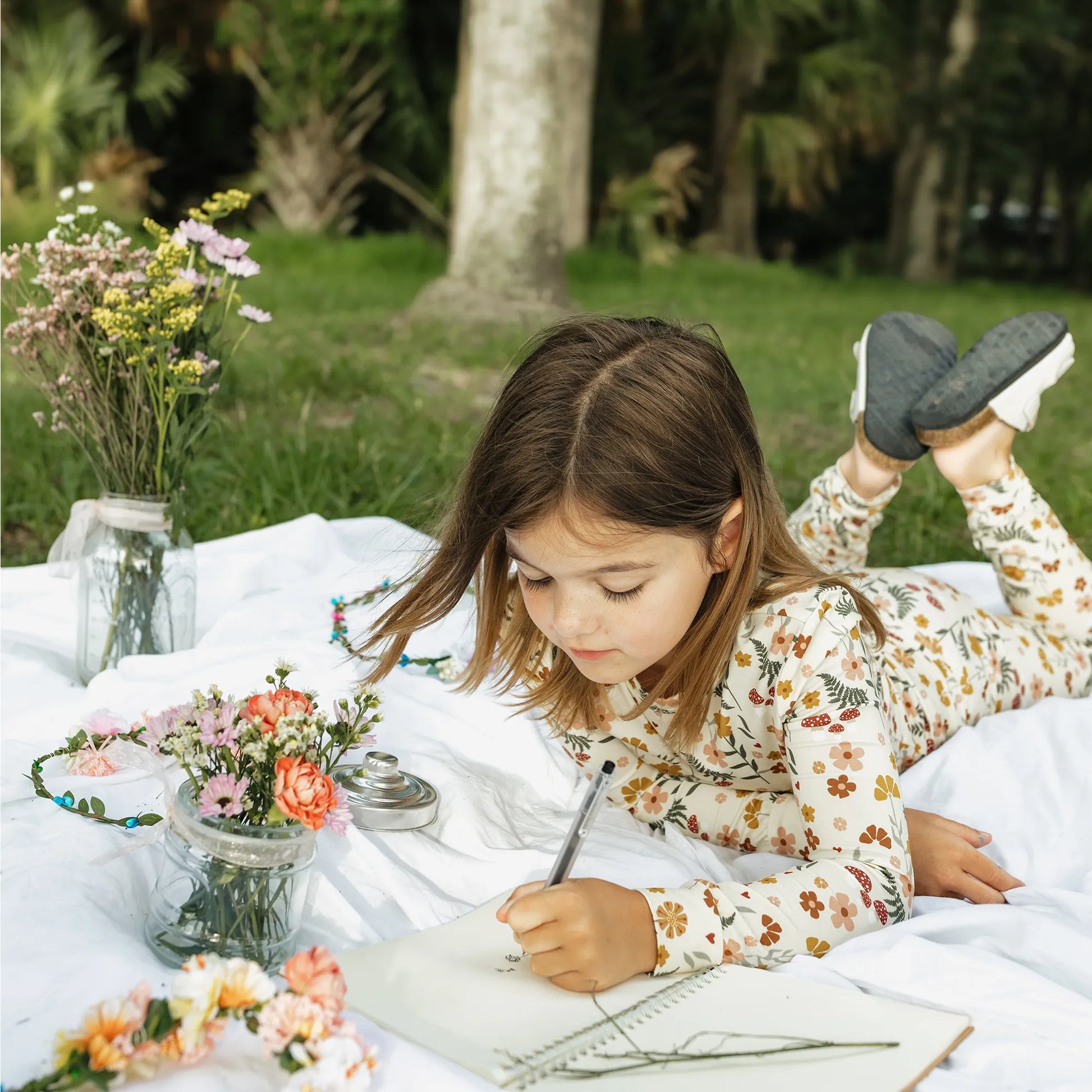 girl wearing cream pj set with floral print on greenery background.