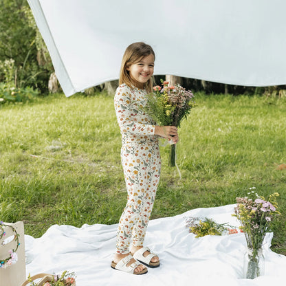 girl wearing cream pj set with floral print on greenery background.