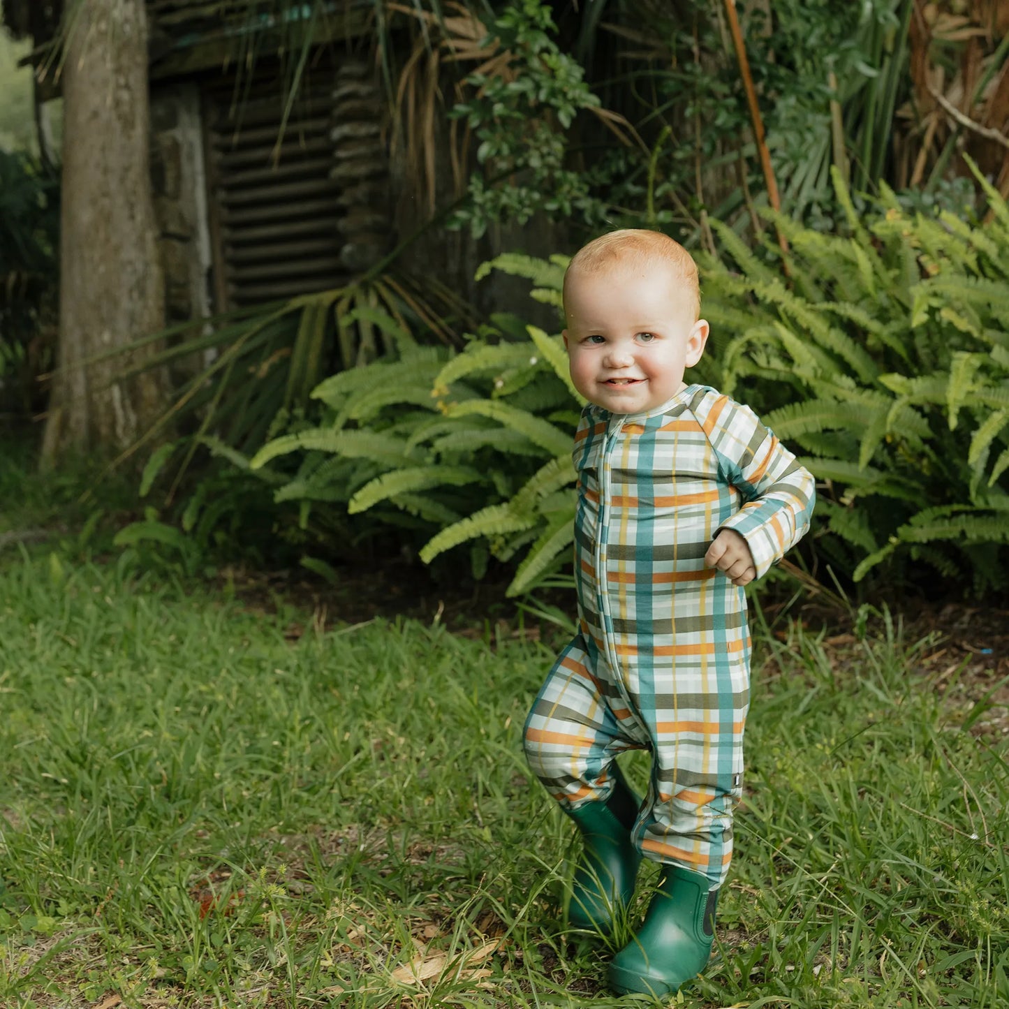 baby wearing fall color plaid zippie on greenery background. 