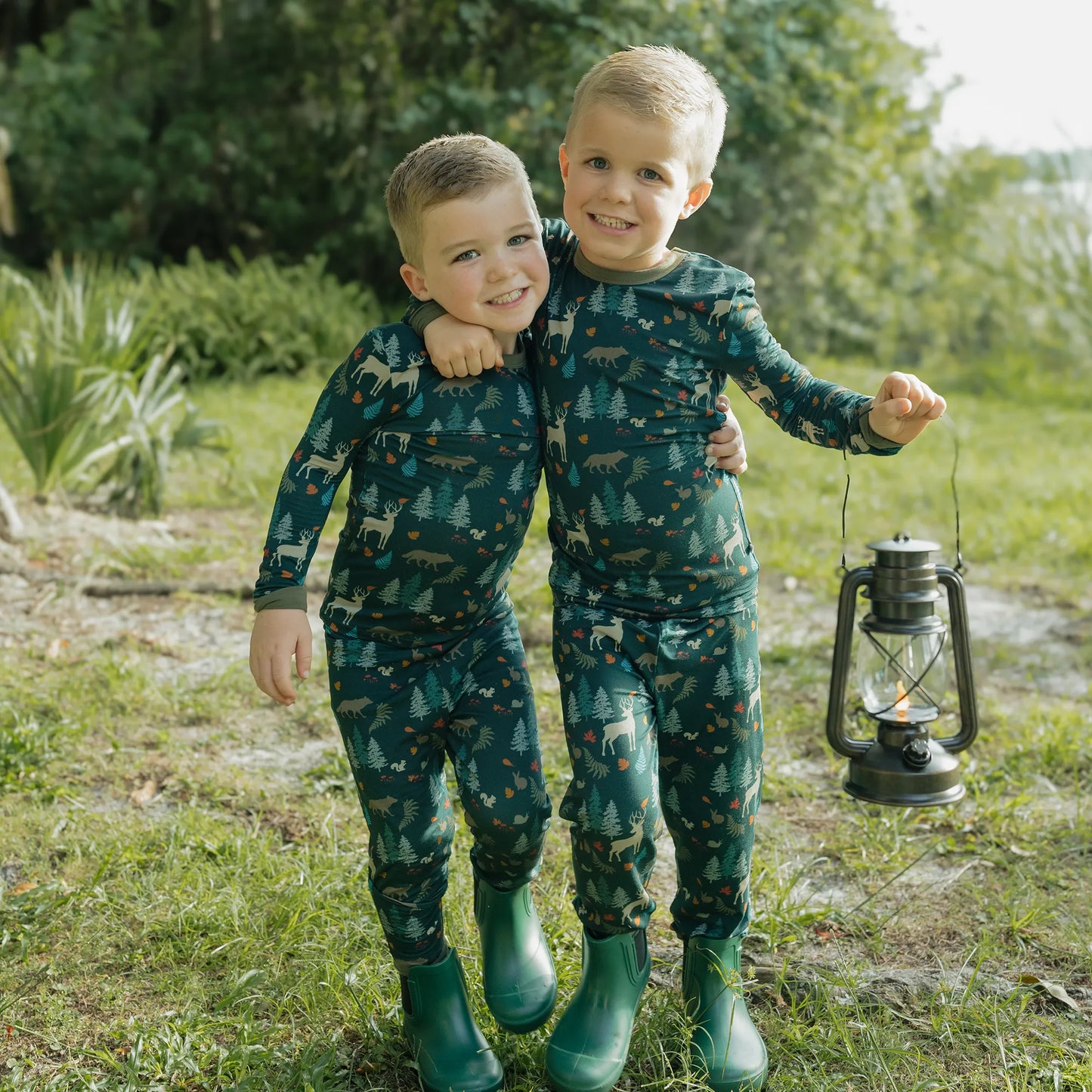 two boys wearing forest print pajama set on greenery background. 