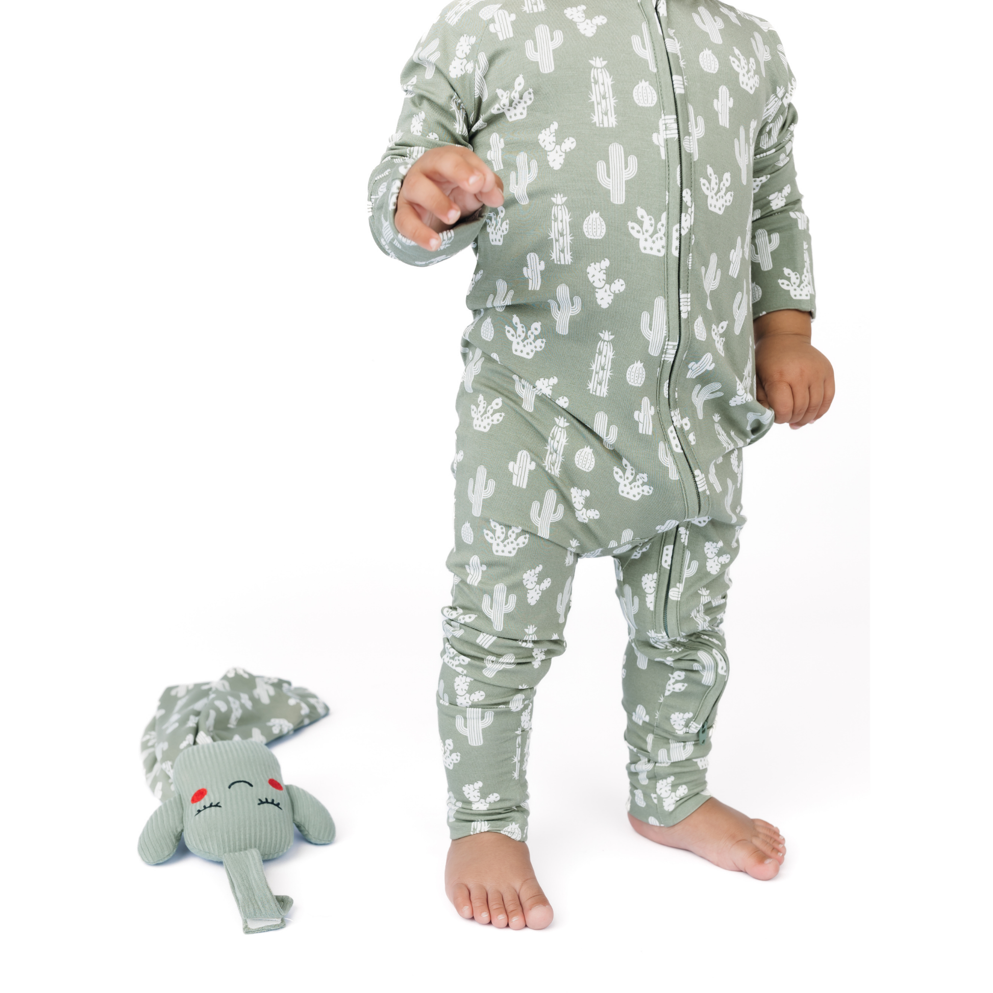 Child wearing a green cactus-patterned onesie with a matching plush toy on a white background