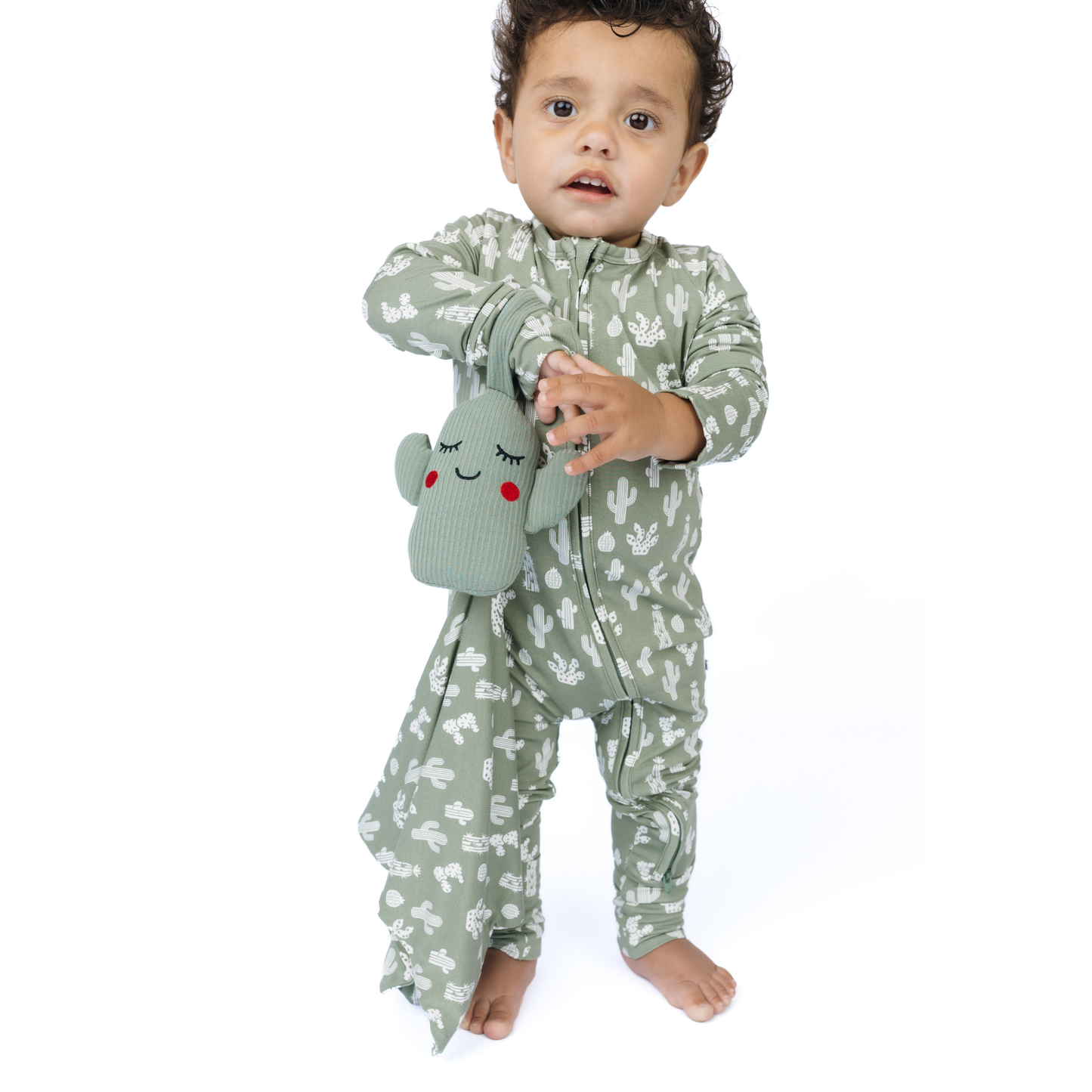 Baby in green floral outfit holding a matching lovey on a white background