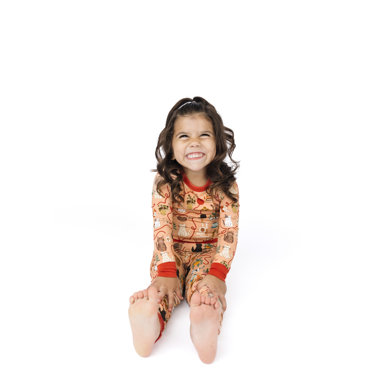 Child wearing a colorful cat pajama set with a pattern, sitting on a white background