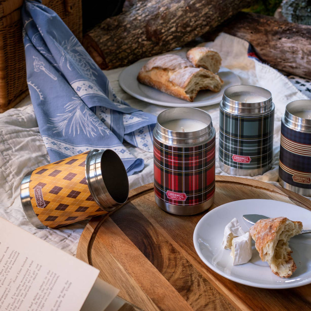 Picnic setup with thermos flasks and food on a wooden tray outdoors.