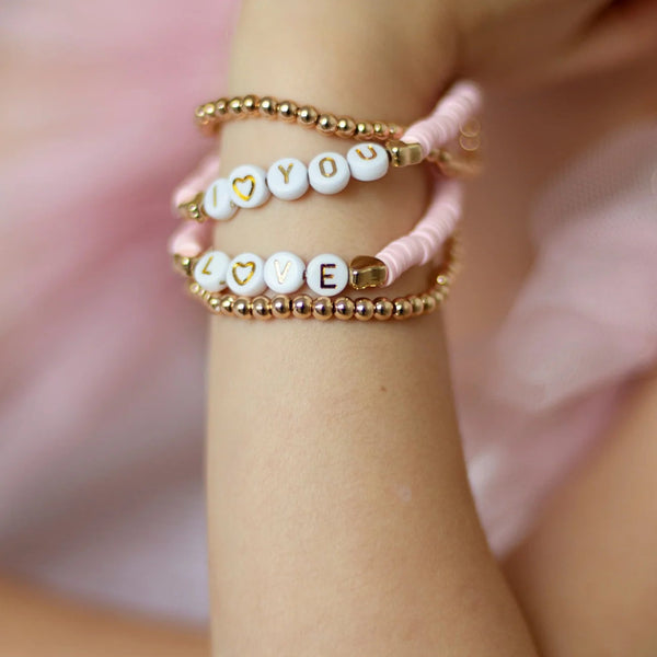 Close-up of a child's wrist wearing four pink, gold and white beaded bracelets that say "I love you" and "Love" from Great Pretenders