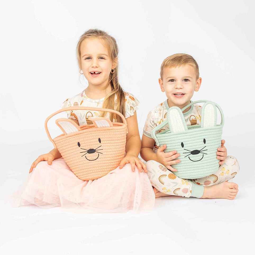 Two toddler sitting on the floor holding the pink and blue bunny baskets.  