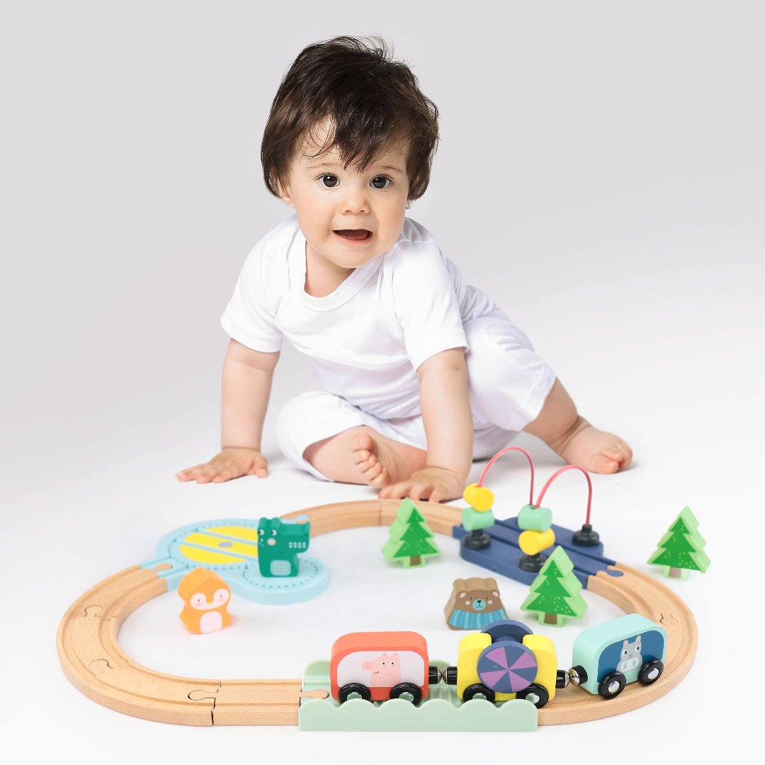 little baby sitting in front of a wooden train set