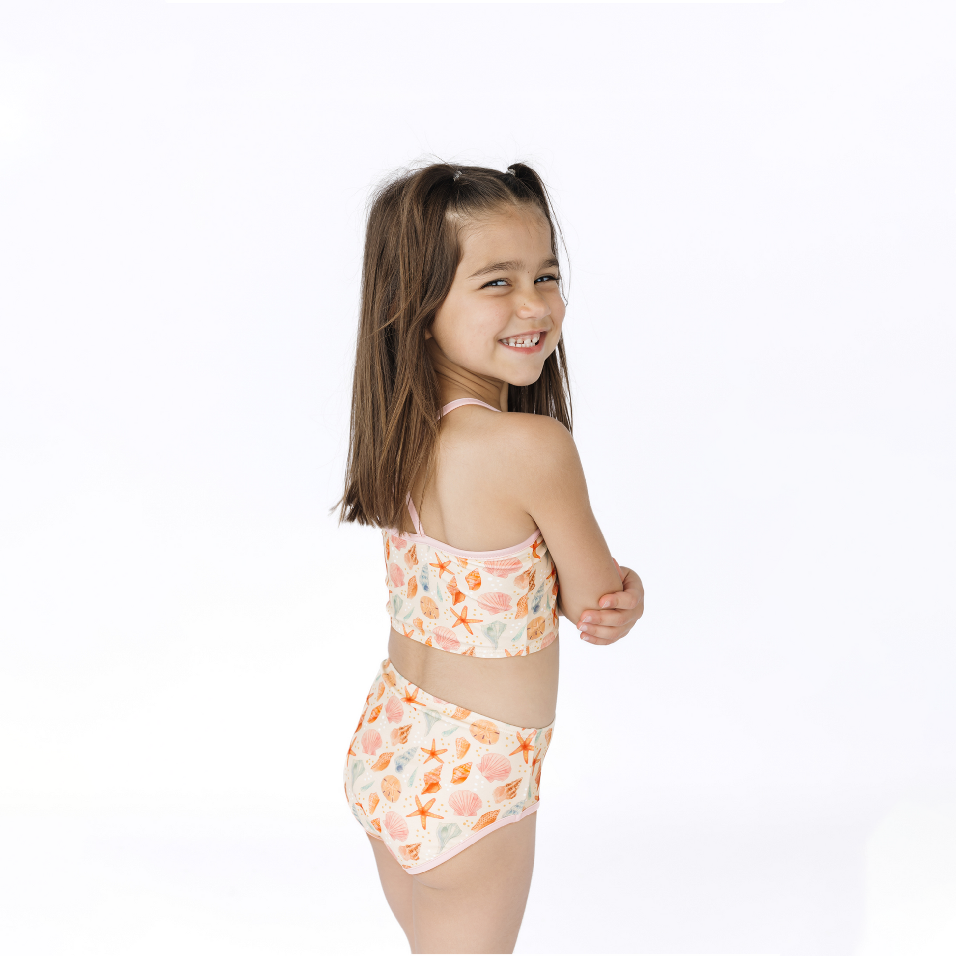 Young girl wearing a seashell two-piece swimsuit on a white background