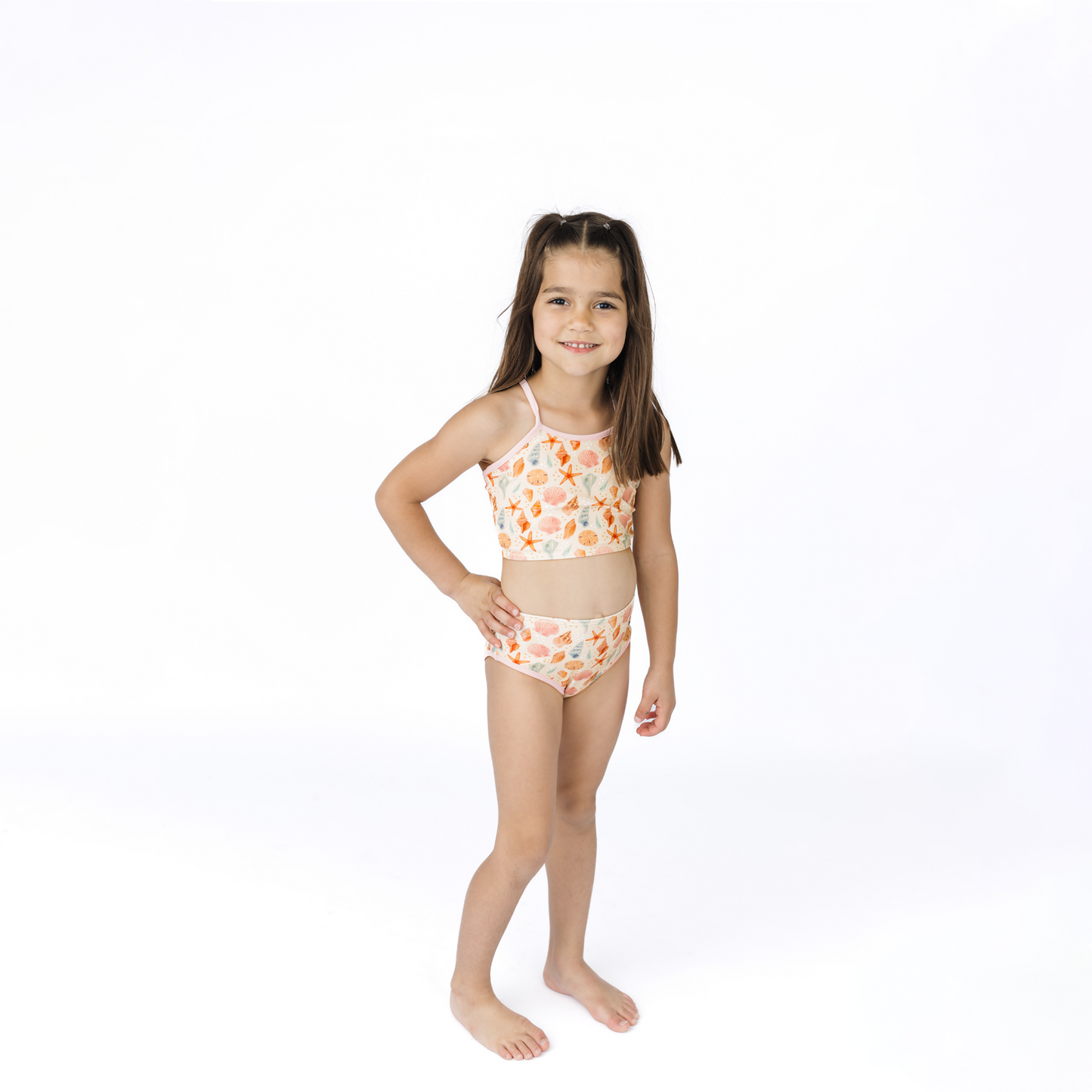 Young girl wearing a two-piece swimsuit with a seashell pattern on a white background