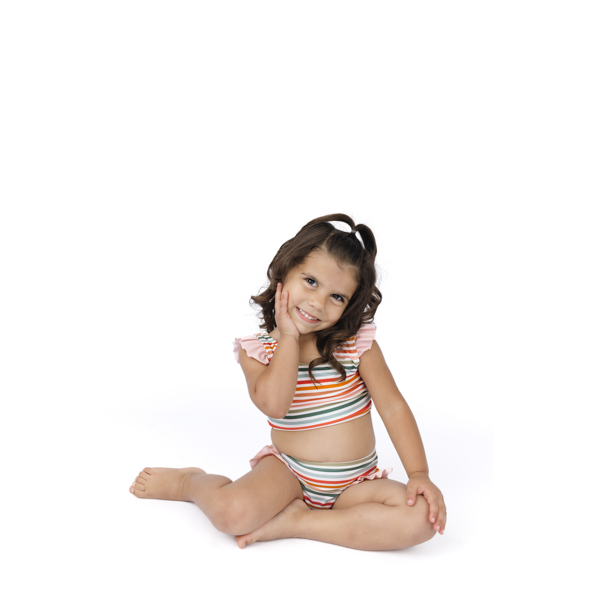 Young girl in a striped swimsuit sitting on a white background