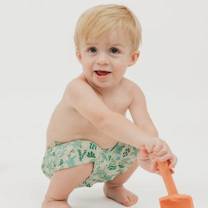 Smiling boy wearing our Save the Sea Turtle Swim trunks. The print is featuring a sea-green turtle and ocean-inspired print. Made from quick-dry, lightweight fabric with an adjustable drawstring waist for a comfy fit. Perfect for beach days and poolside fun!