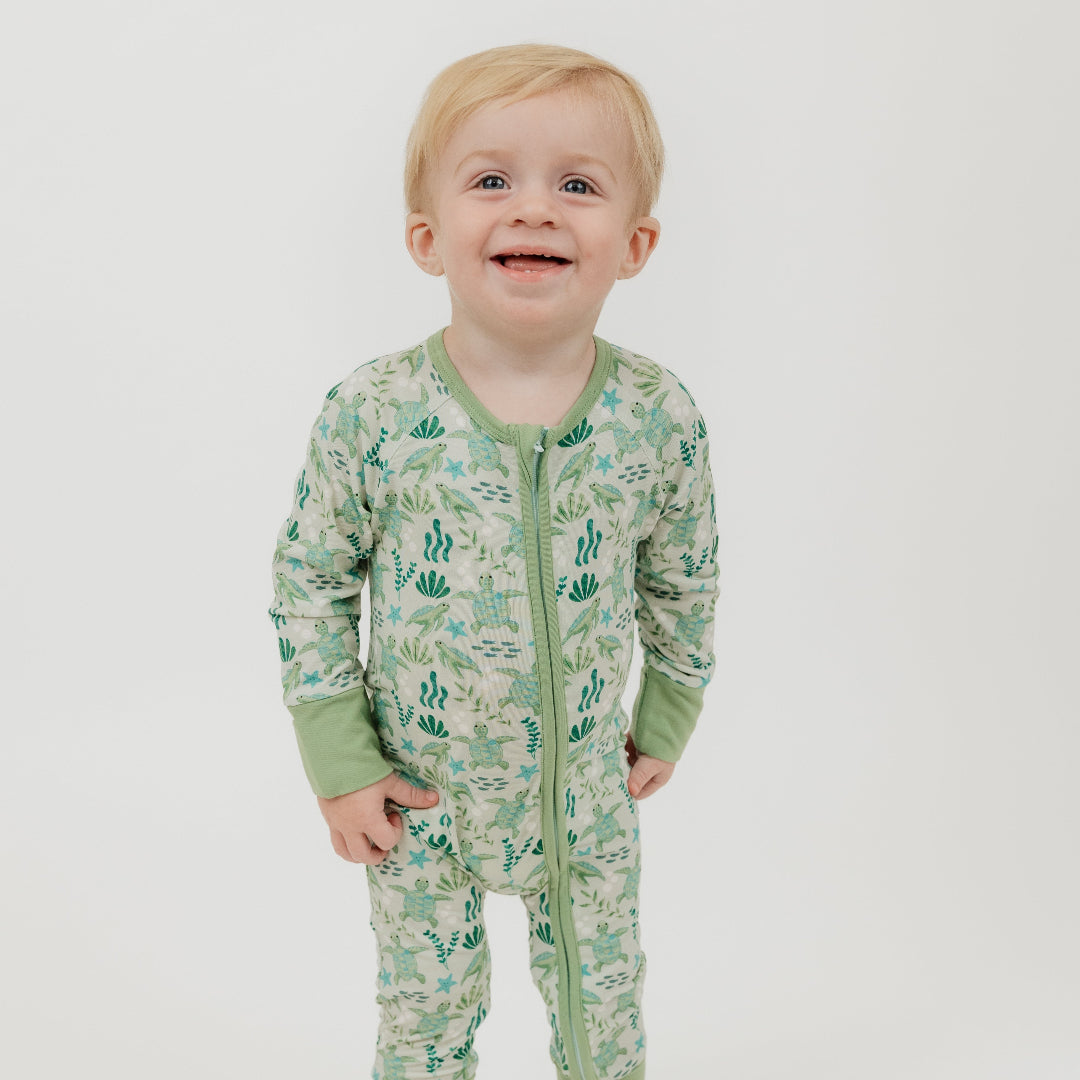 Baby boy wearing our Save the Sea Turtles bamboo convertible baby pajamas by Emerson and Friends. This ultra-soft, eco-friendly footie features a charming sea turtle and ocean-inspired print. Made from breathable bamboo fabric, it’s perfect for sensitive skin and designed for ultimate comfort with fold-over feet and mittens.