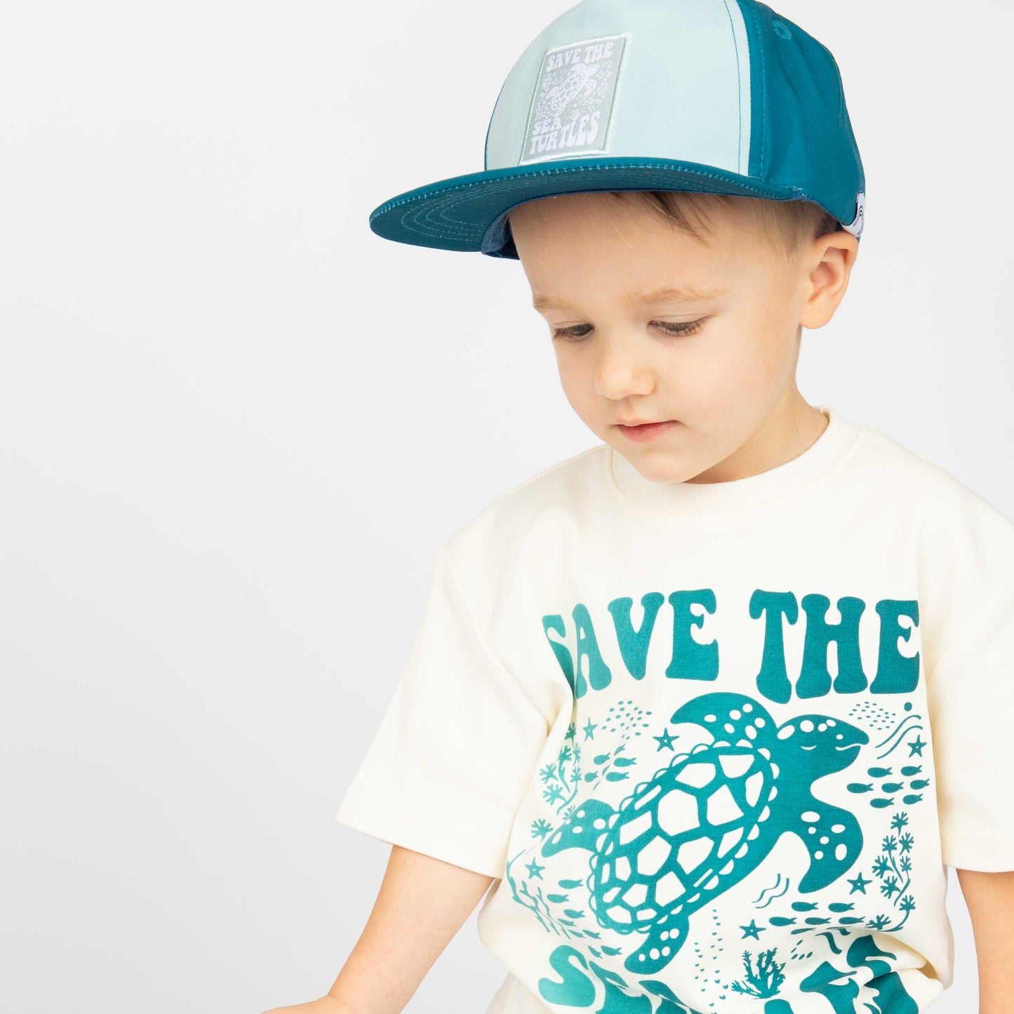 A young boy wearing pieces from our Save the Sea Turtle collection, including the hat and cotton t shirt on a white background. 