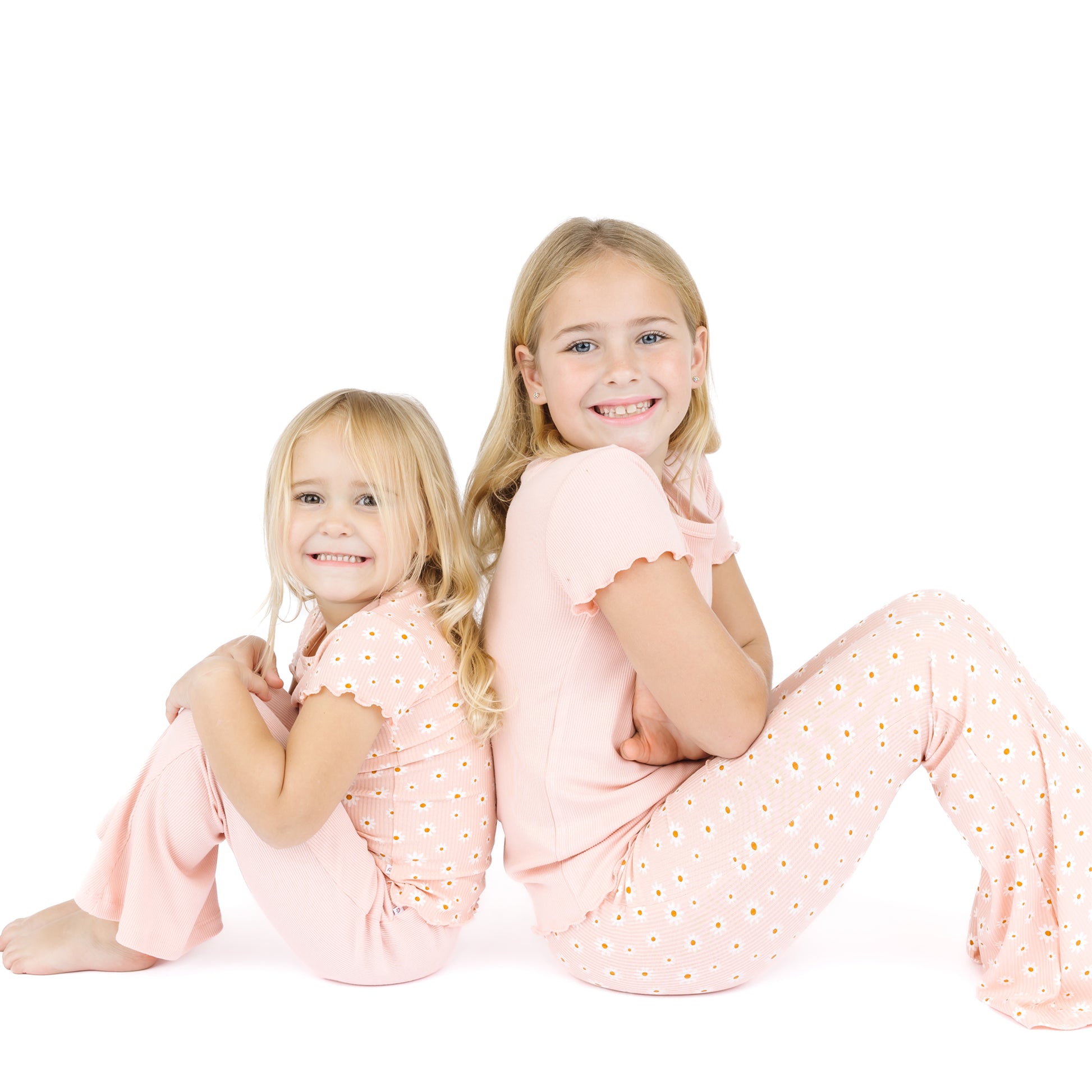 Two young girls wearing matching pink pajamas with a white background
