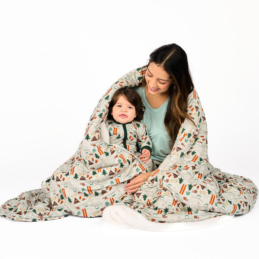 Mother and daughter modeling in white background wearing bamboo pajama ski day featuring trees, cabins, and other ski activities wearing a blanket