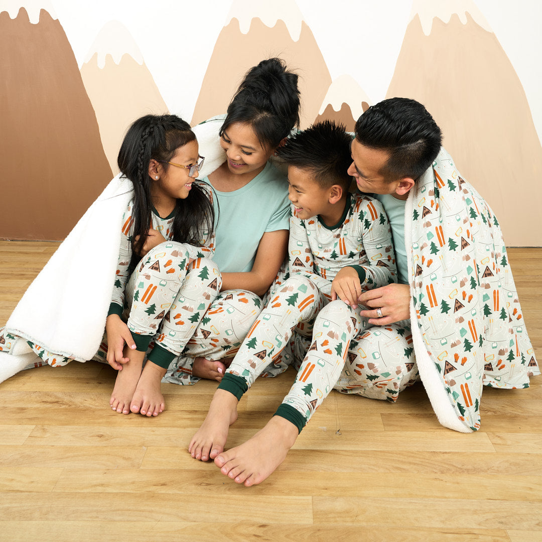 Family modeling in white background wearing bamboo pajama ski day featuring trees, cabins, and other ski activities.