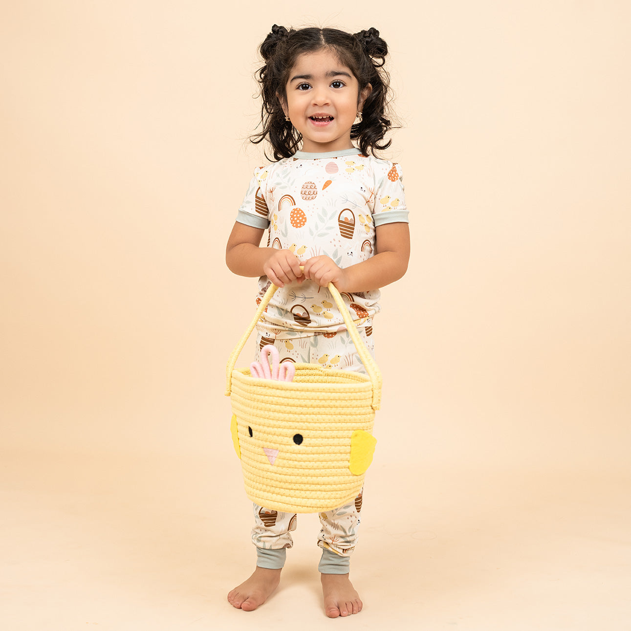 Little girl standing up holding our Chicks Easter Basket in our two piece hop to it pajamas that features bunnies, chicks, easter eggs and more!