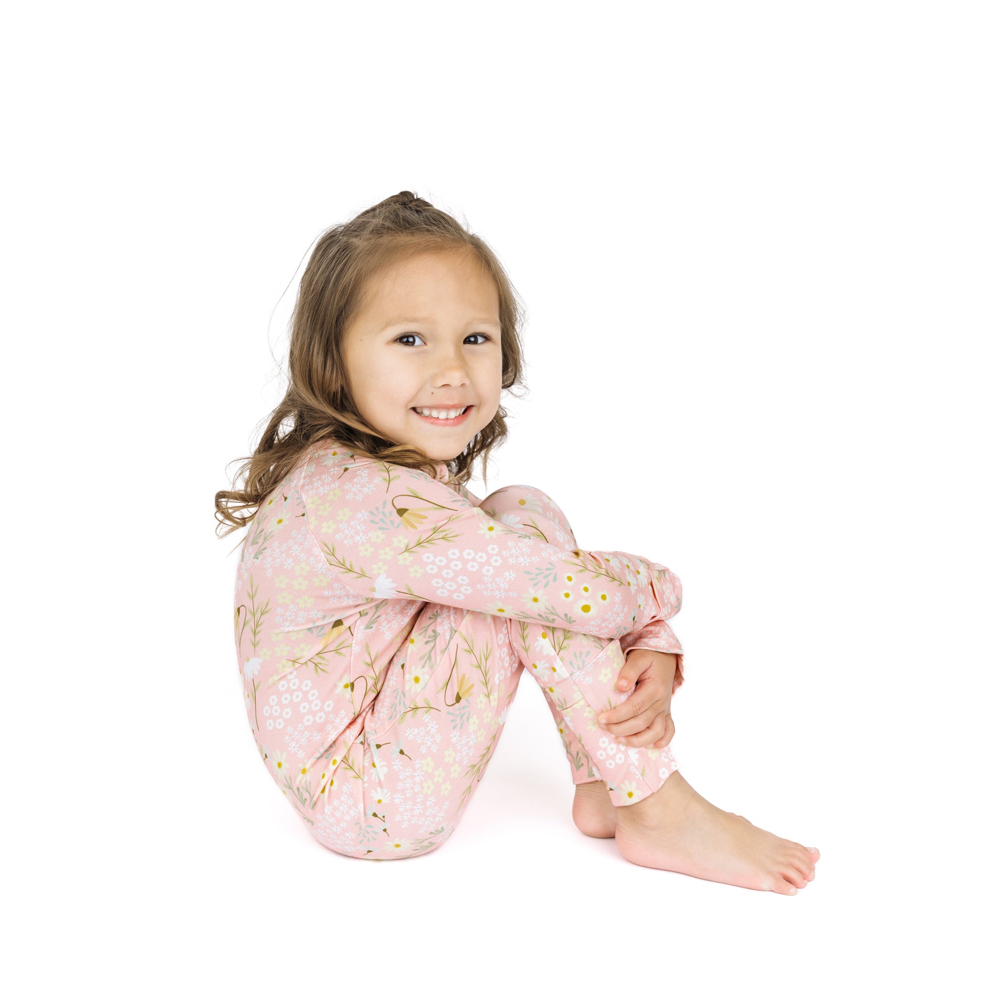 Young girl wearing pink floral pajamas sitting on a white background
