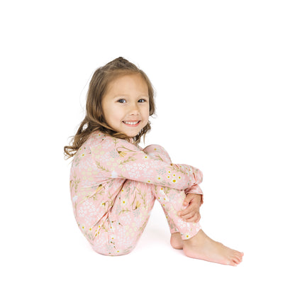 Young girl wearing pink floral pajamas sitting on a white background