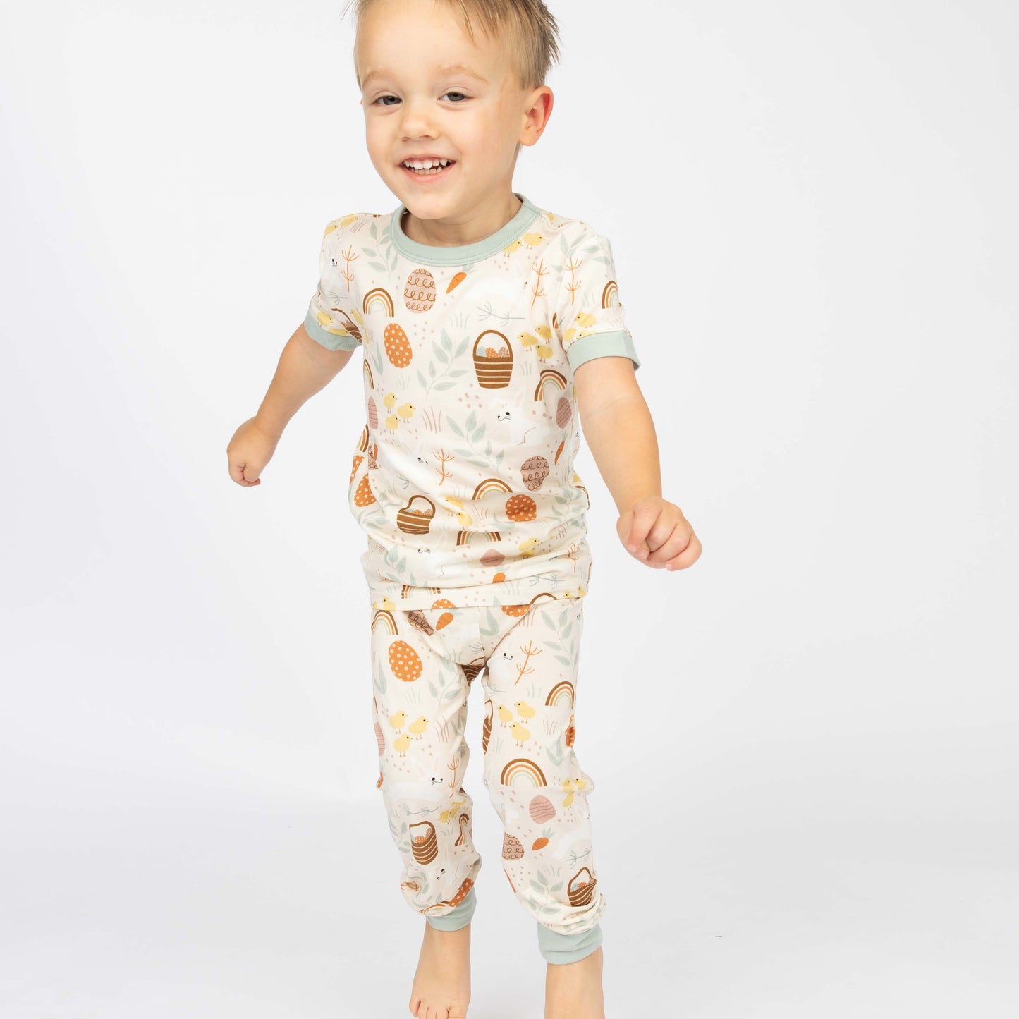 Little boy smiling in his two piece bamboo pajama set. The print features easter eggs, bunnies, chicks and more!