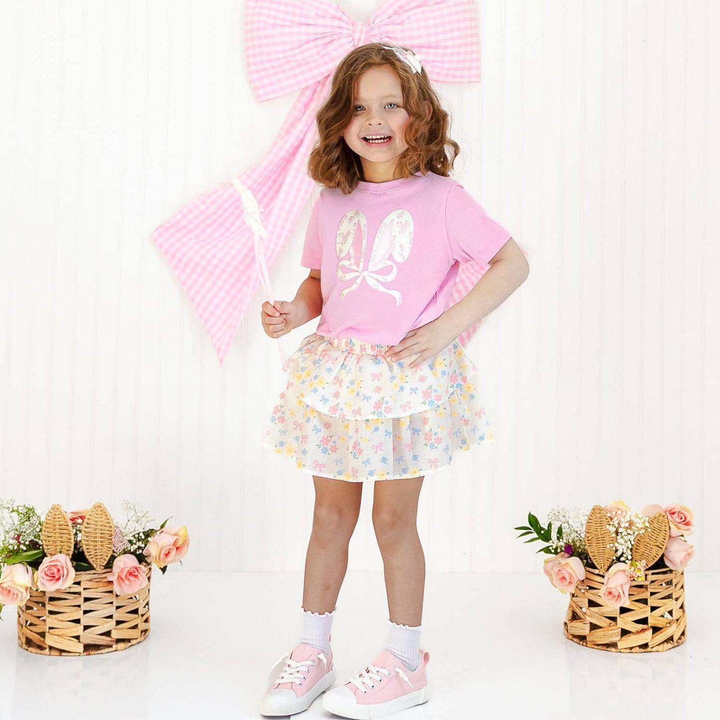 Young girl in a pink outfit with floral skirt and shoes, holding a pink umbrella on a white background.