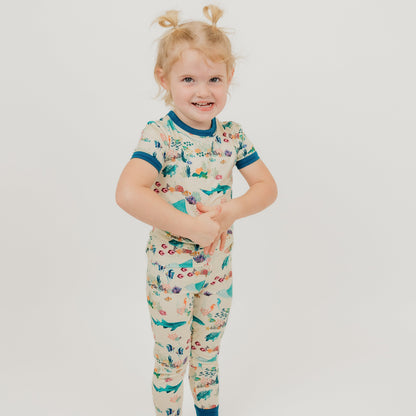 Toddler girl wearing Emerson and Friends Coral Reef Bamboo Kids Pajama Set featuring a soft, breathable short sleeve top and matching pants with an ocean-inspired print of sharks, sea turtles, and coral reefs—perfect for cozy nights and sweet dreams.