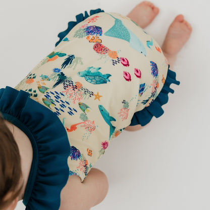 Close up of baby girl crawling in a white background wearing our Emerson and Friends Coral Reef Ruffle Leg One Piece Girls Swimsuit, featuring a vibrant ocean-inspired print with sharks, sea turtles, and coral, designed with adorable ruffle accents and a secure fit for fun beach and pool days.