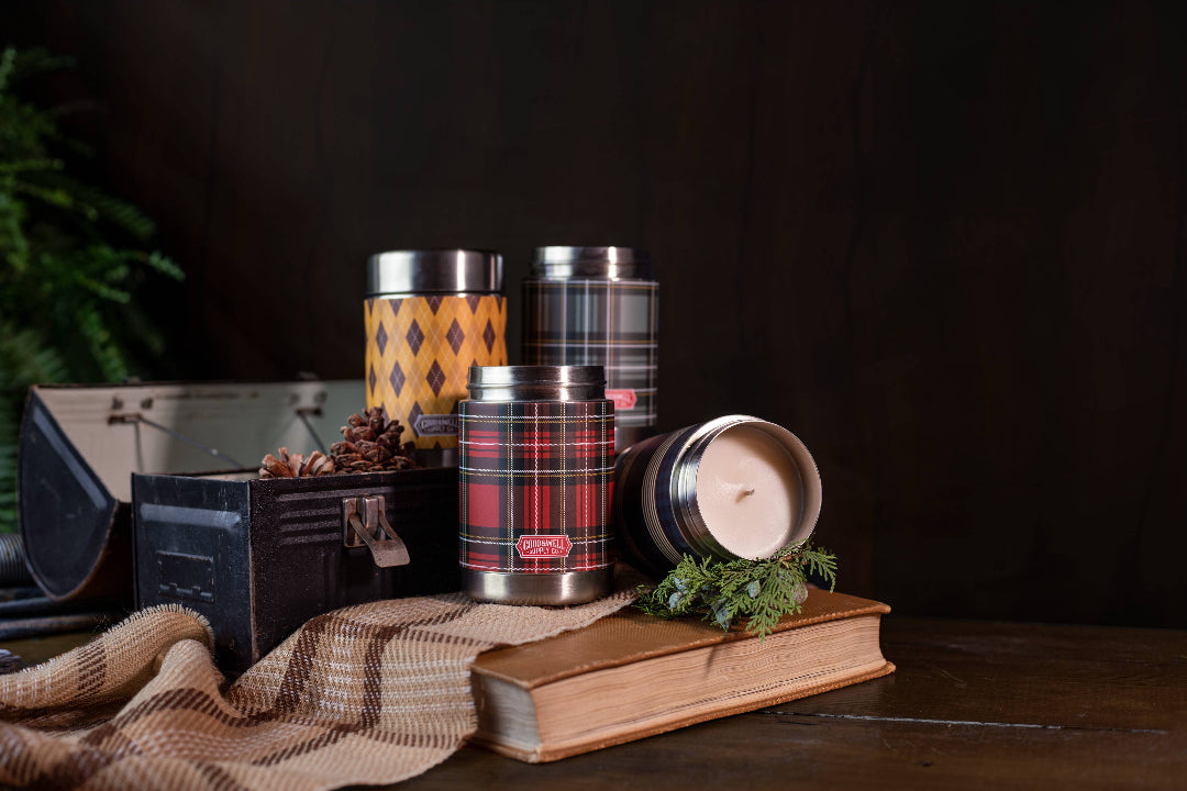 Collection of plaid-patterned tins and a candle on a wooden surface with a dark background