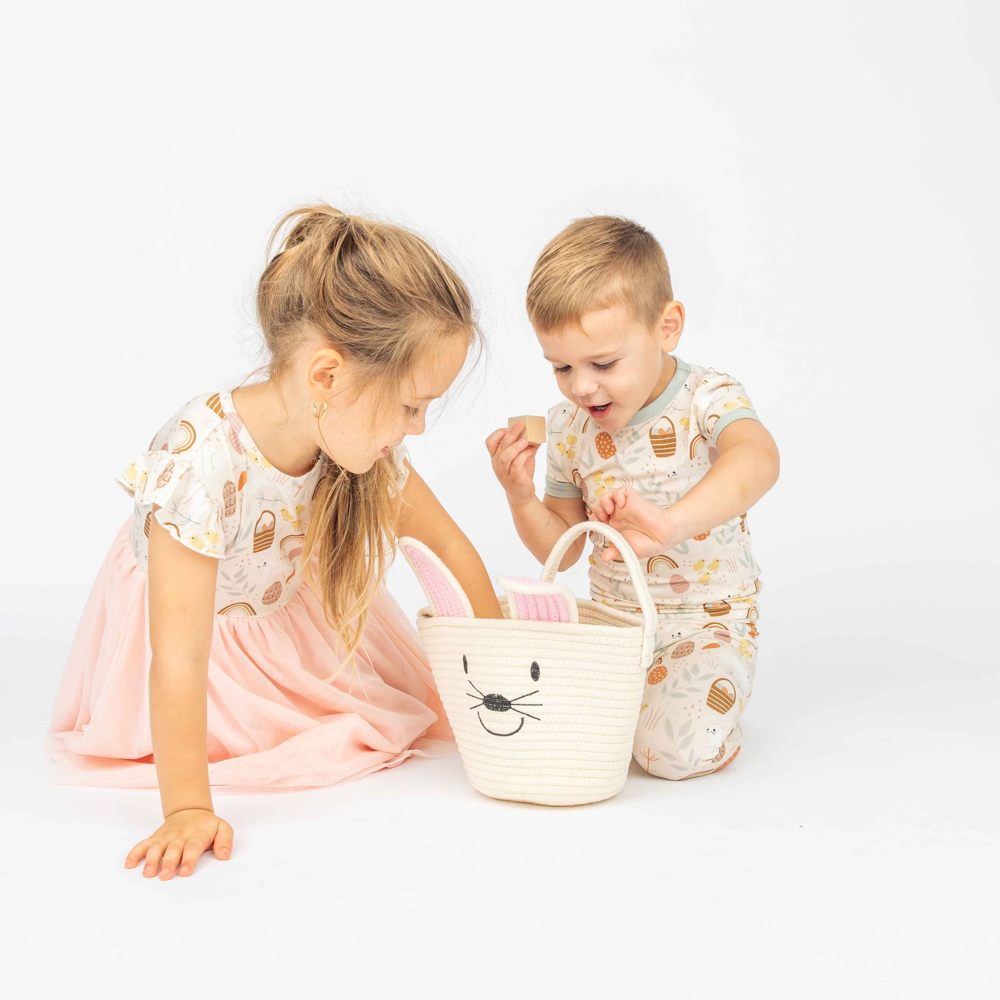 Kids sitting down and playing, looking over a white bunny basket.