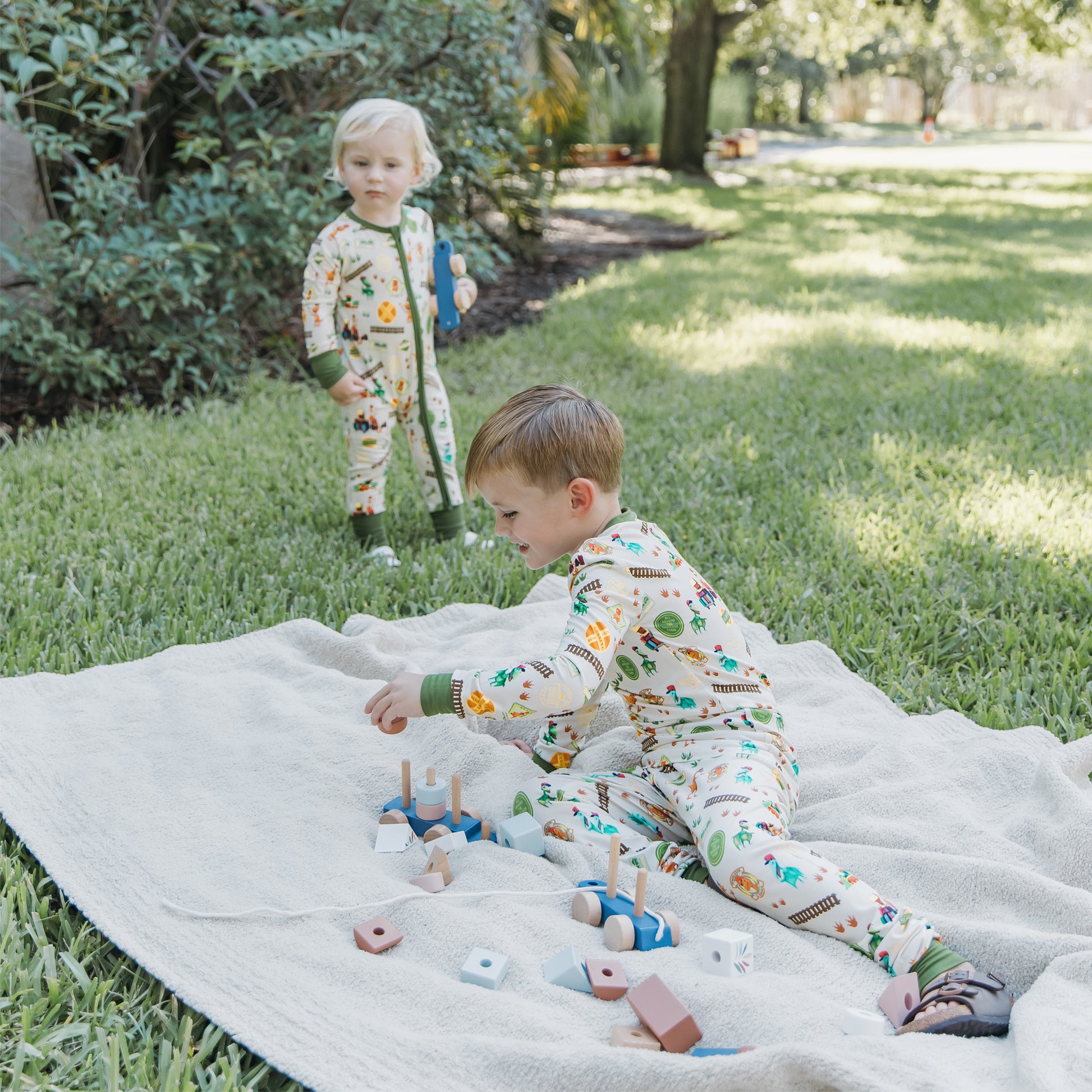 Two children wearing All Aboard the Dinosaur Train™ bamboo pajamas playing together outdoors