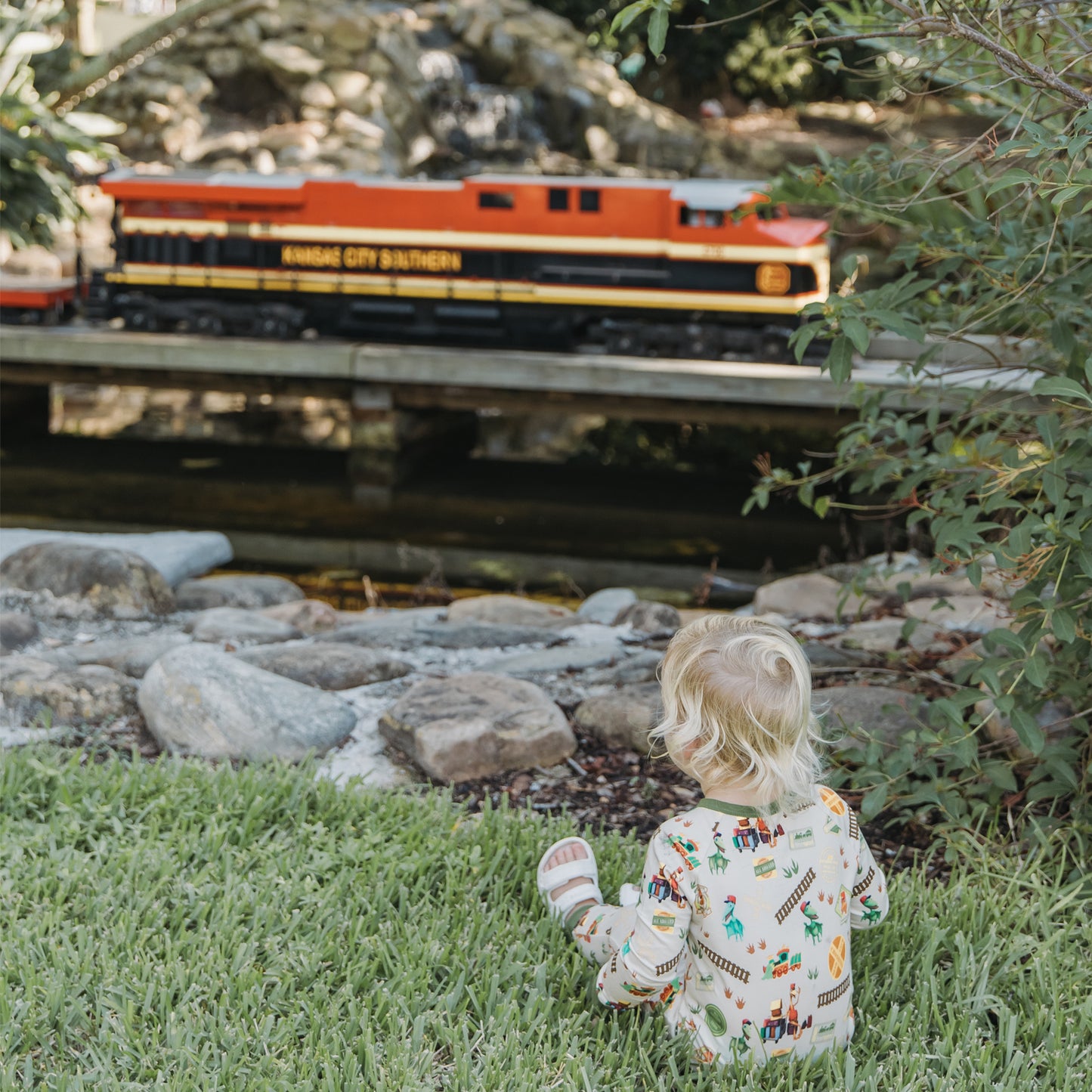 Child in All Aboard the Dinosaur Train™ bamboo convertible pajamas watching a toy train outdoors
