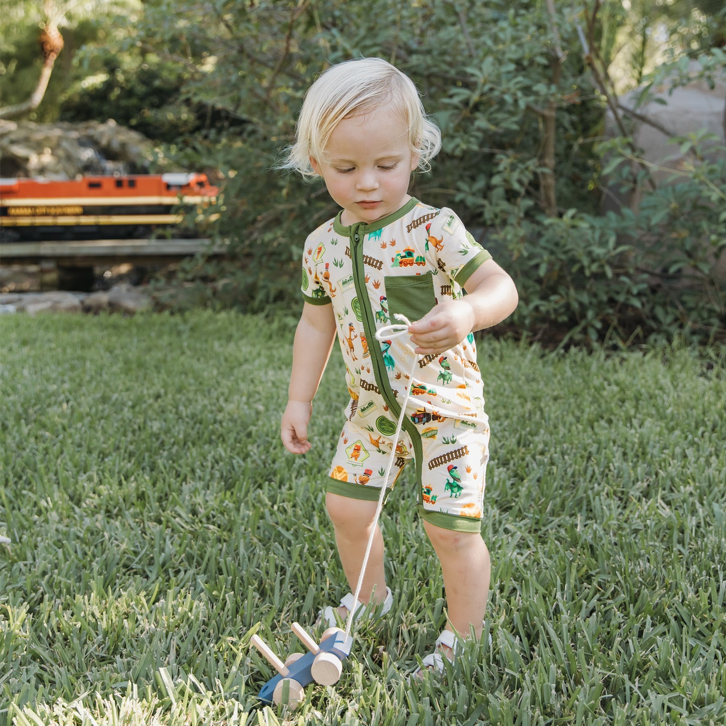 Baby wearing All Aboard the Dinosaur Train™ bamboo romper standing on the grass outdoors