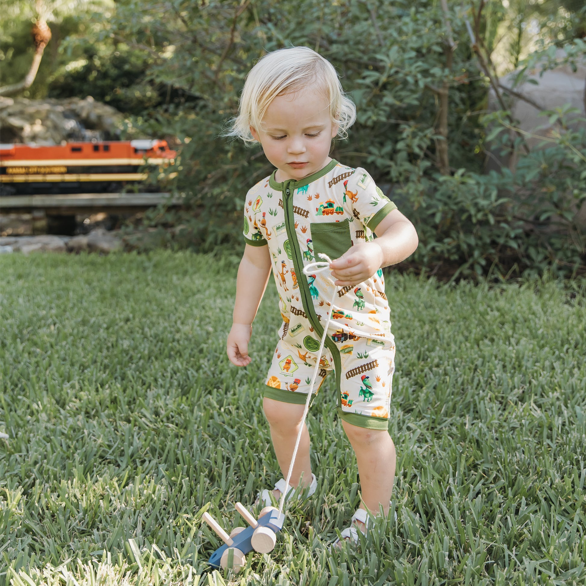 Baby wearing All Aboard the Dinosaur Train™ bamboo romper standing on the grass outdoors