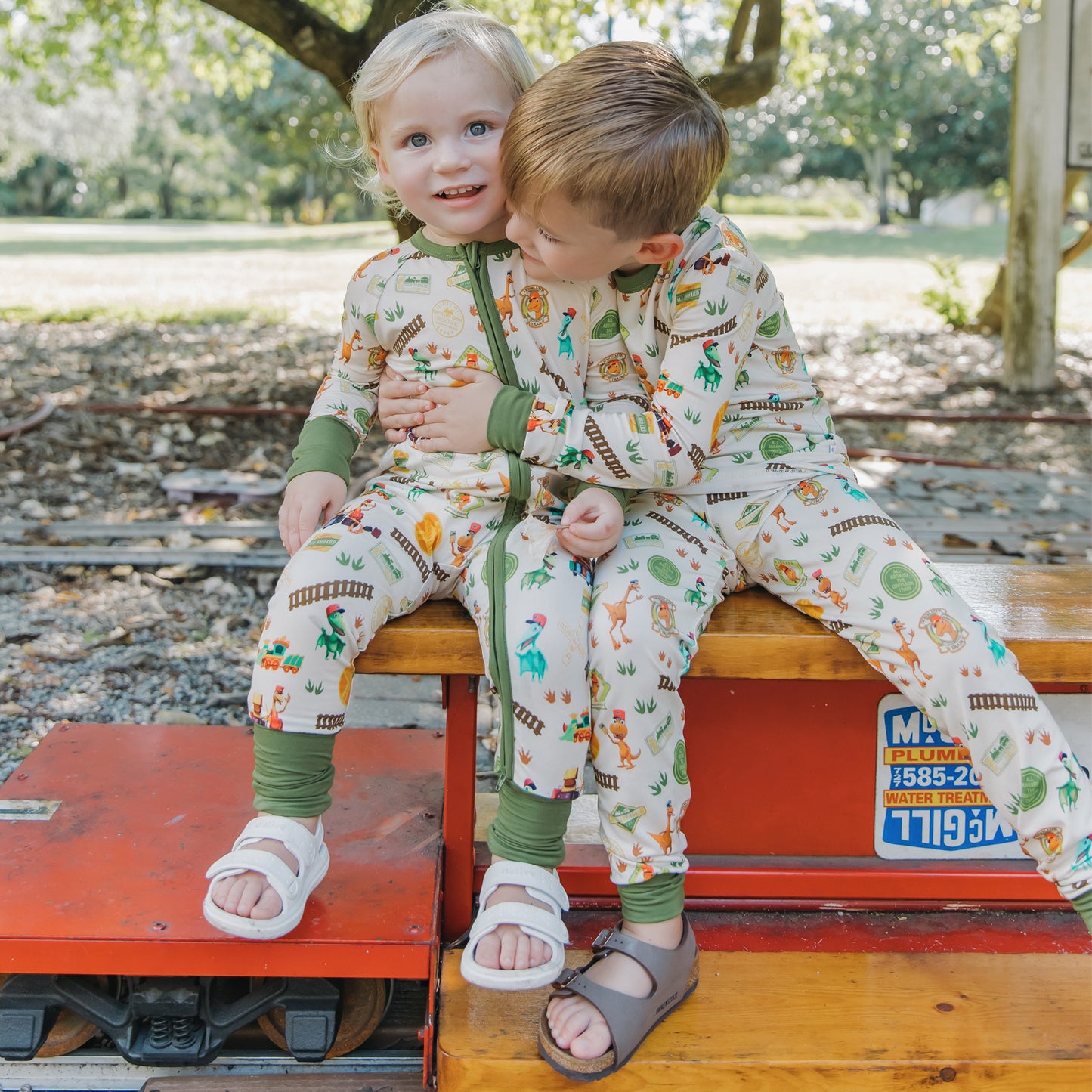 Two brothers wearing matching All Aboard the Dinosaur Train™ bamboo pajamas sitting together
