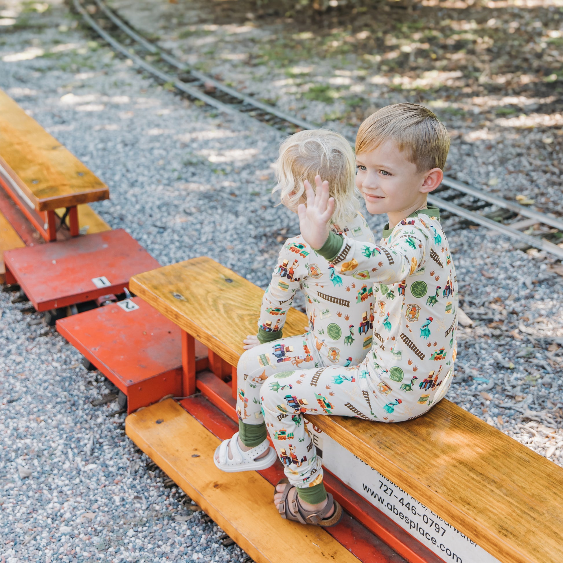 Two boys wearing All Aboard the Dinosaur Train™ bamboo pajamas playing near a toy train outdoors
