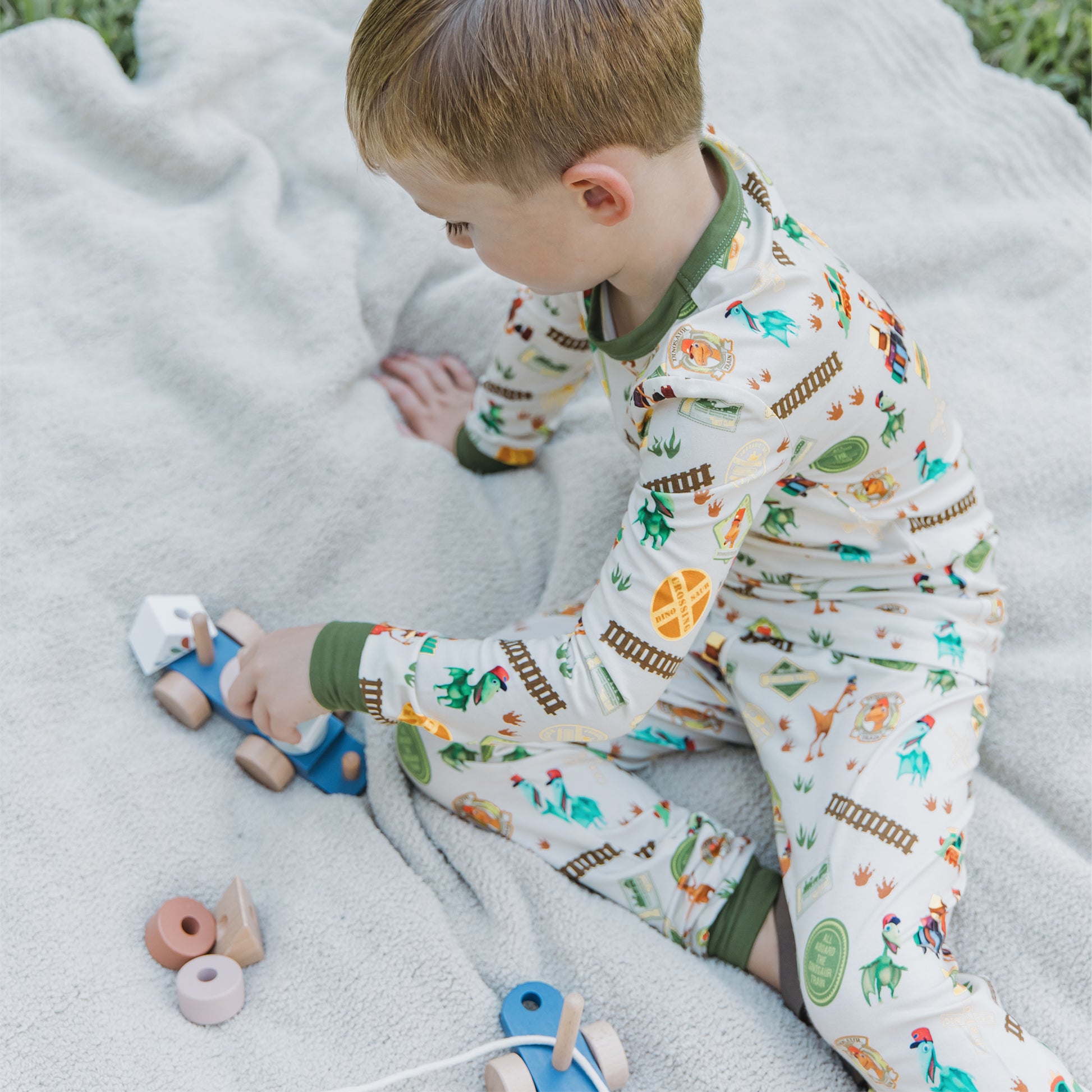 Toddler wearing All Aboard the Dinosaur Train™ bamboo pajamas playing in the blanket. 