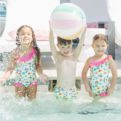 Siblings playing in the pool with our Arthur's Family Vacation one piece and swim trunks with a playful print of Arthur™ in swimwear surrounded by fun beach props — perfect for family getaways.