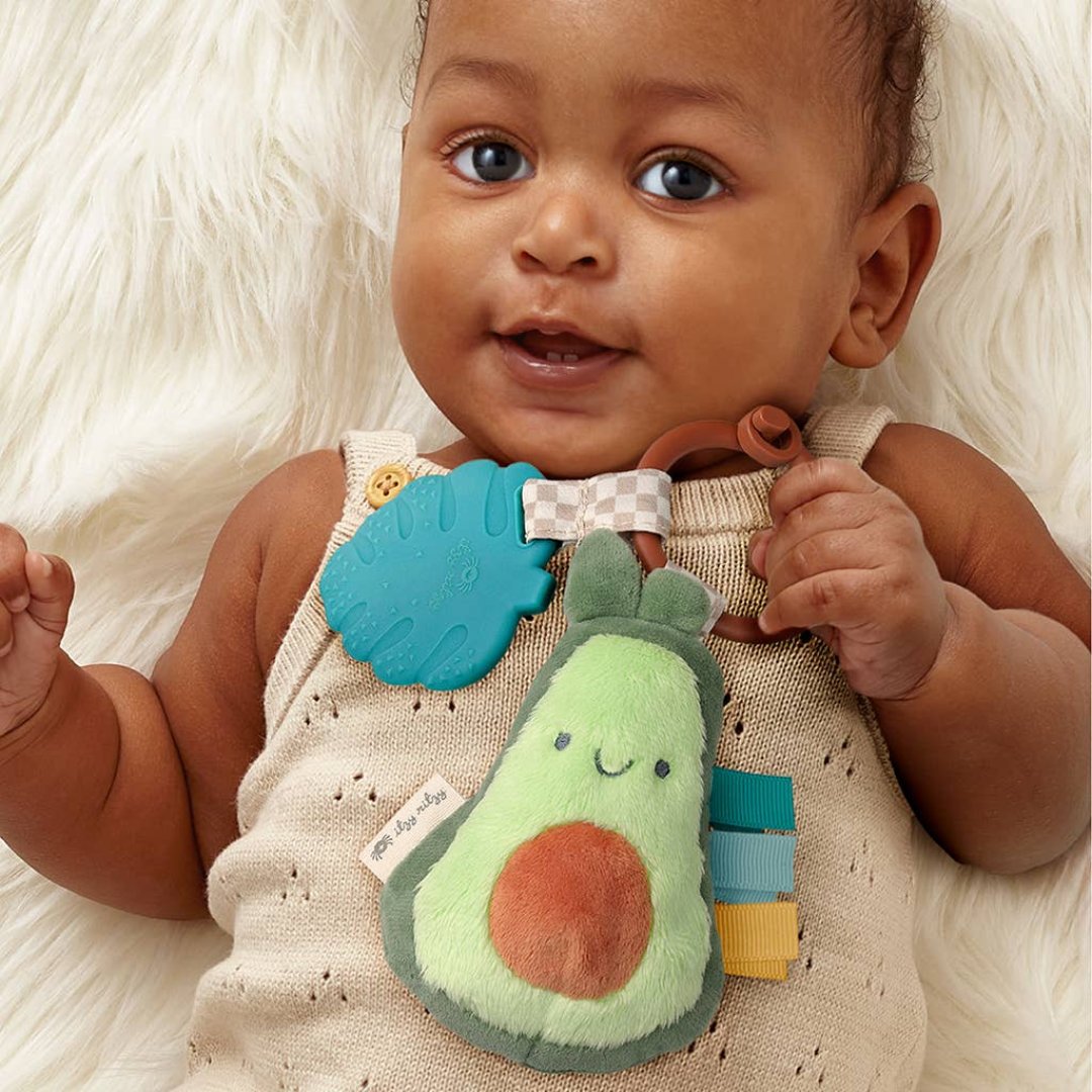 baby holding a stuffed toy avocado with a green leaf teether attached