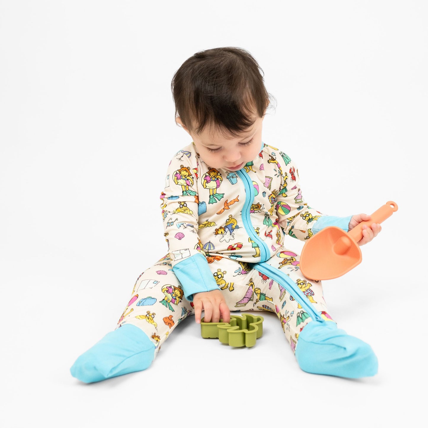 Baby girl wearing our Arthur's Family Vacation Bamboo Convertible Baby Pajamas featuring vibrant light blue trim, a double zipper, and a playful print of Arthur™ in swimwear surrounded by fun beach props — perfect for family getaways.