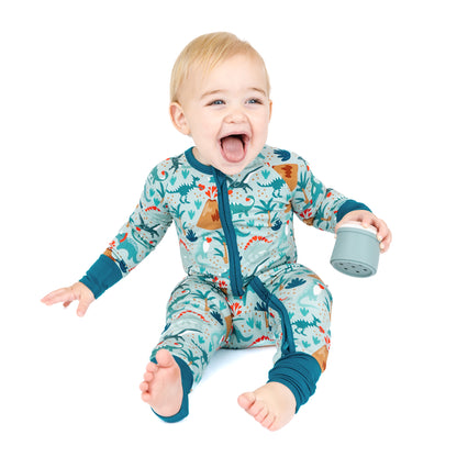 Baby sitting in bamboo zip pajama with playful dinosaur volcano print.