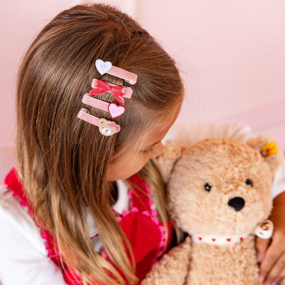 Child with decorative hair clips holding a teddy bear against a pink background