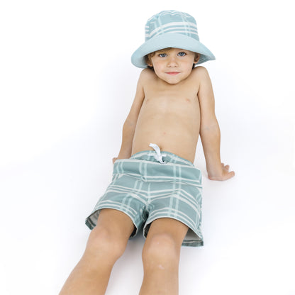 Child wearing a light blue checkered hat and green plaid shorts on a white background