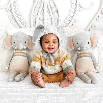 Baby wearing an elephant-themed outfit with two elephant plush toys on a white background