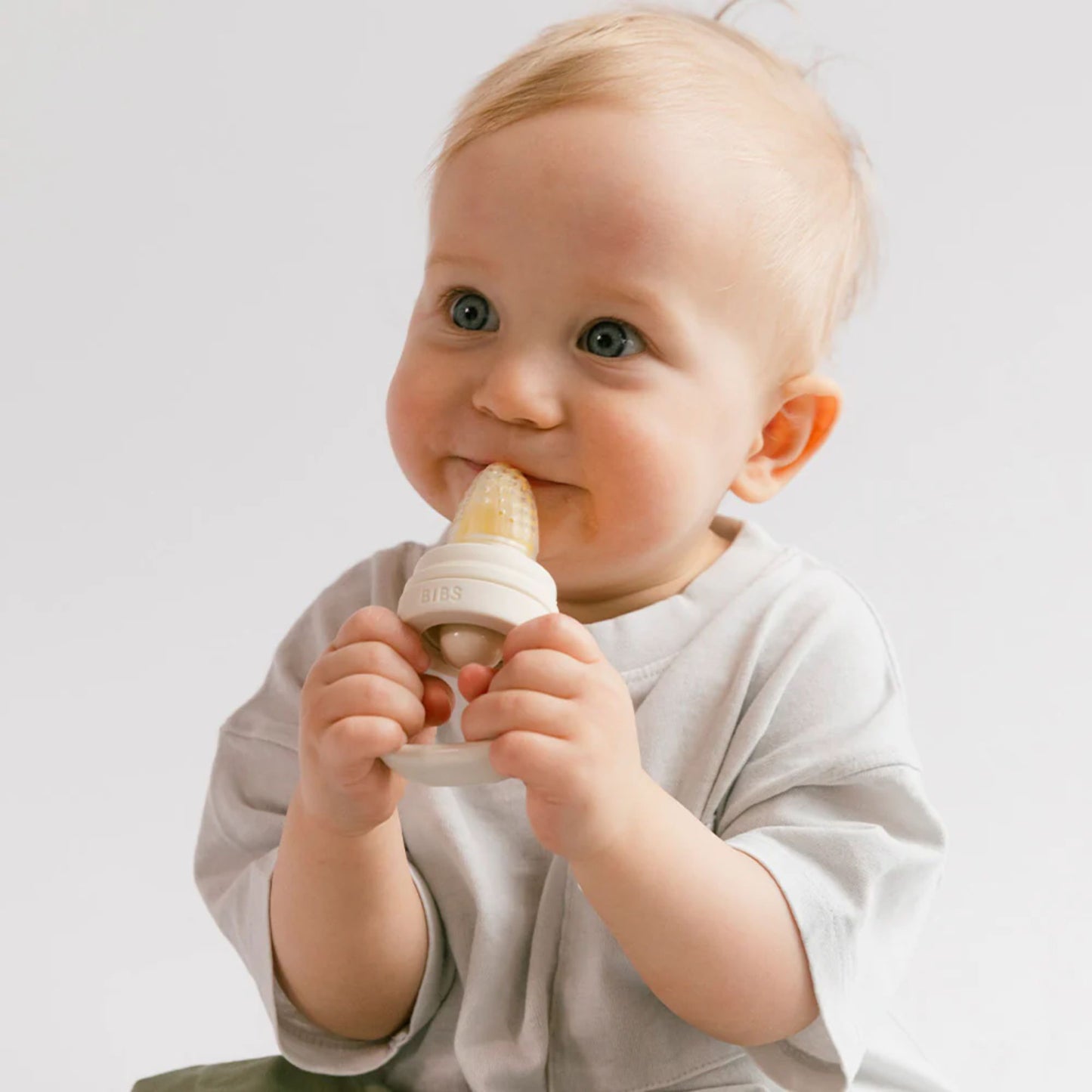 Baby holding a white teething ring against a plain background